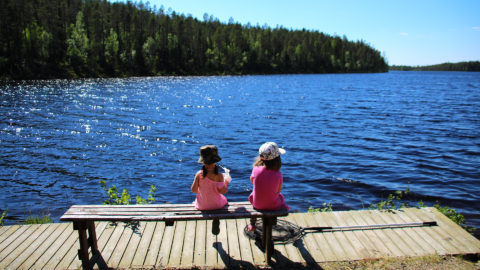 Två flickor på en bänk. De sitter med ryggen mot kameran och tittar över vattnet.