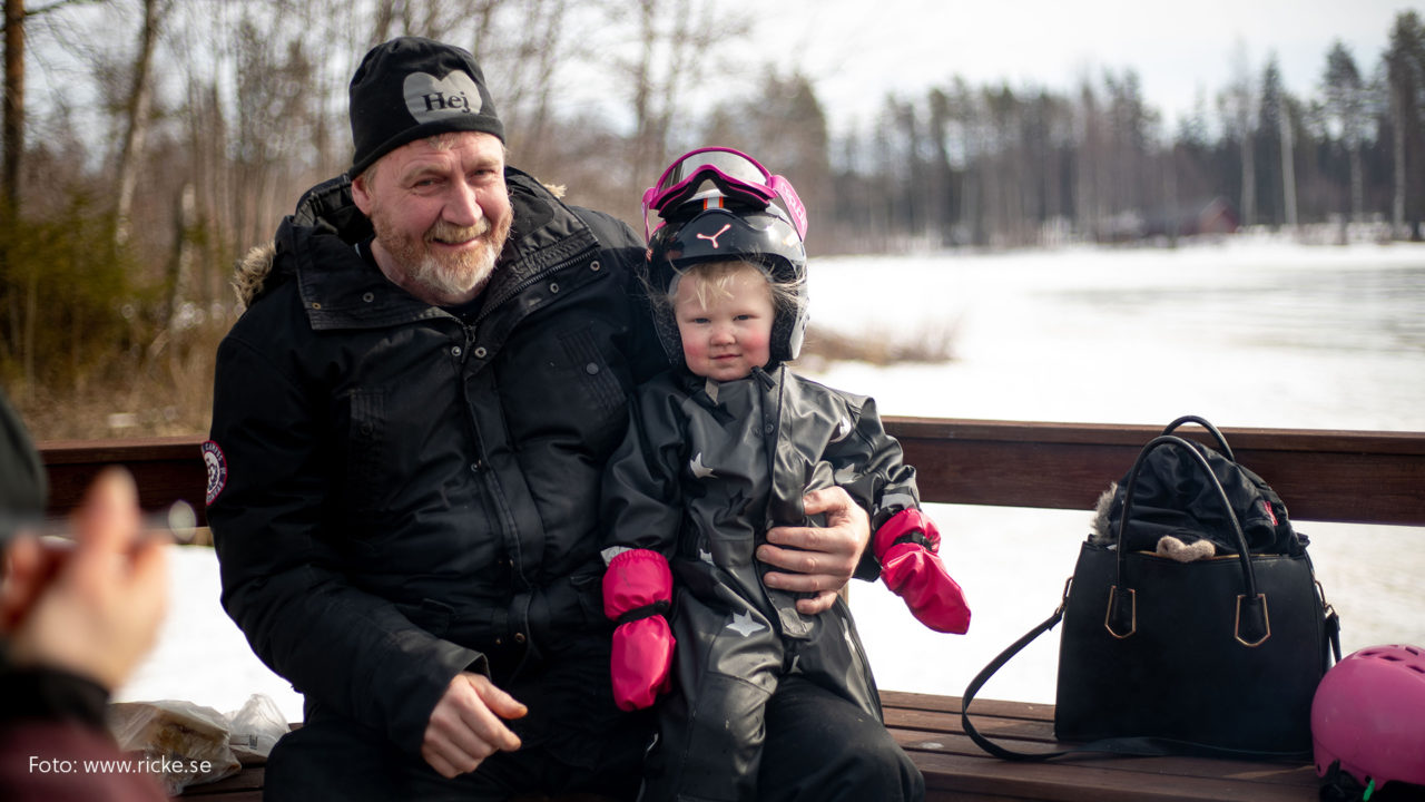 Man med sitt barnbarn i knät. Vinterbild.