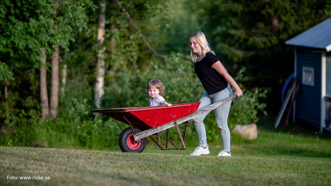 Större tjej som skjutsar yngre i en röd skottkärra.