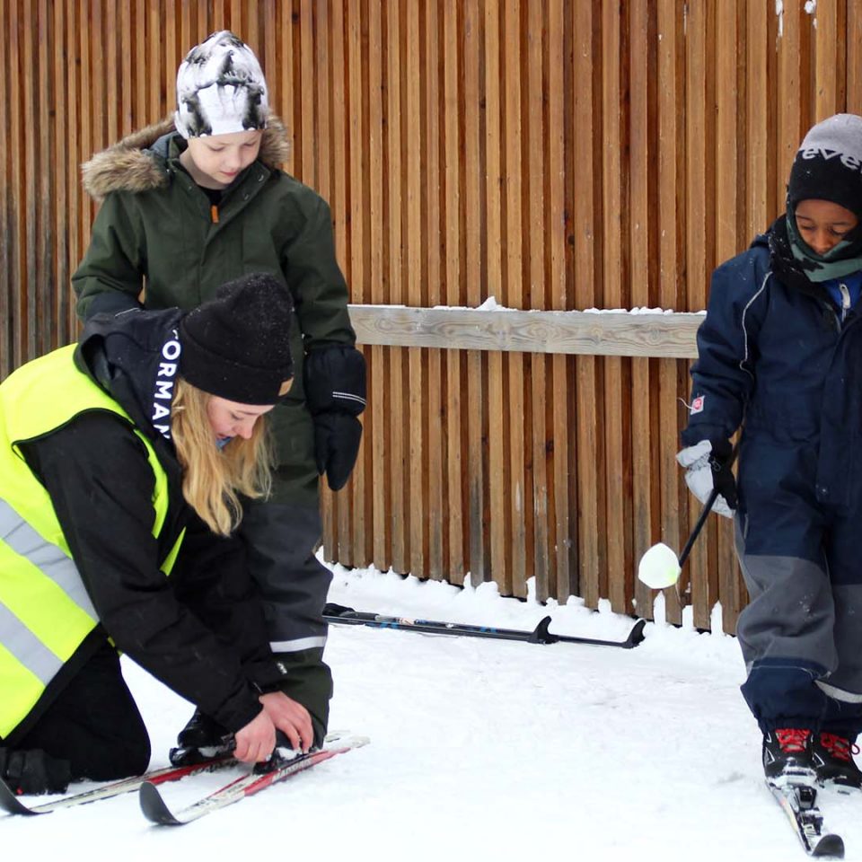 Personal som hjälper ett barn på med skidor.