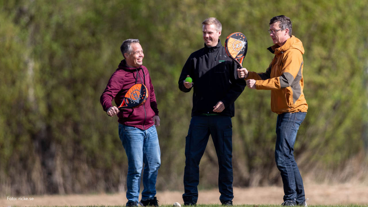 Tre män som håller i var sitt padelracket. De ser glada ut.