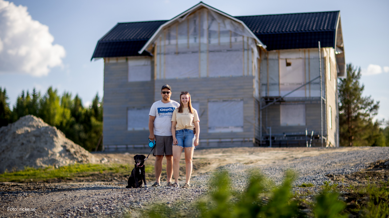 En man, kvinna och en hund framför ett hus som byggs.